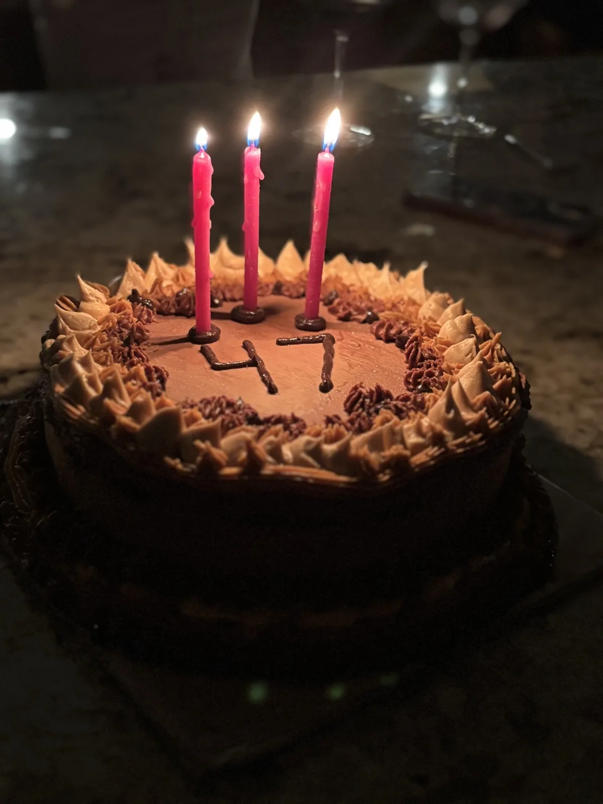 Chocolate '47' birthday cake with a piped border and three lit candles