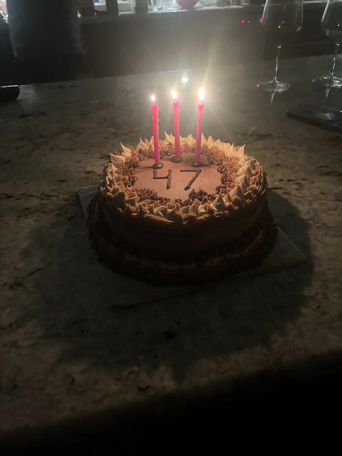 Chocolate '47' birthday cake with a rosette border and three lit candles, candlelit