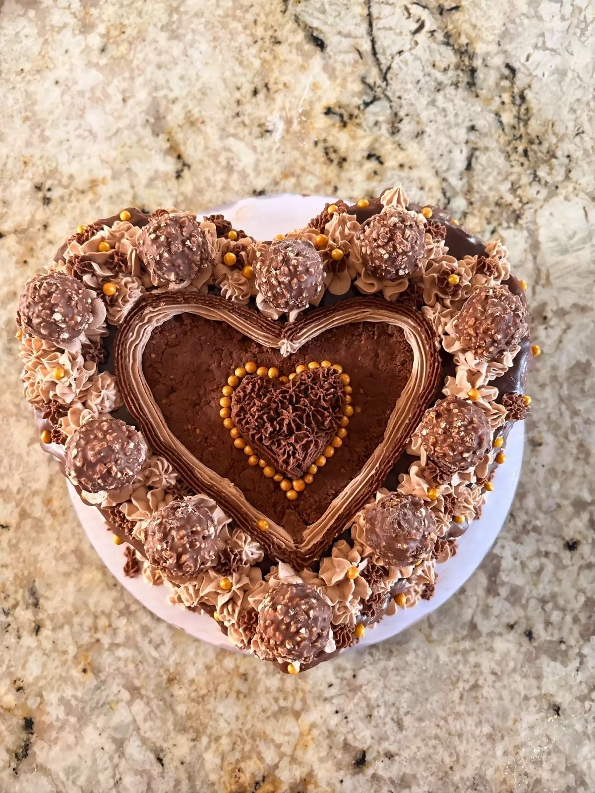 Heart-shaped chocolate hazelnut cake topped with chocolate hazelnut candies and gold pearls