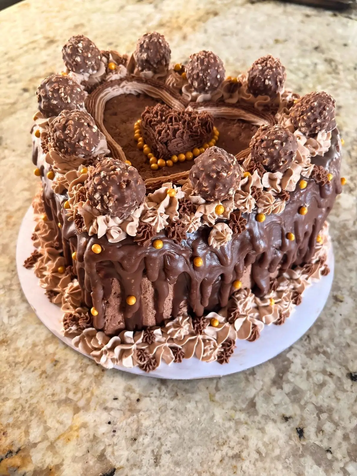 Heart-shaped chocolate hazelnut cake with chocolate hazelnut candies, gold pearls, and a chocolate drip