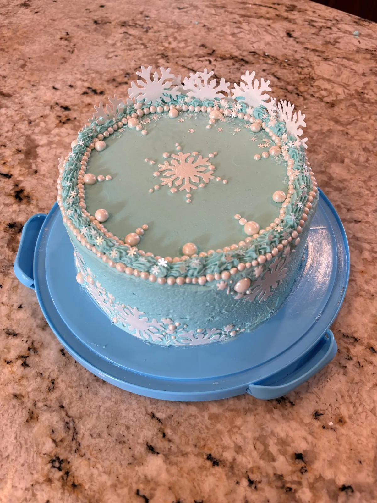 Ice blue buttercream cake trimmed with white sugar pearls, white snowflakes, and a piped border