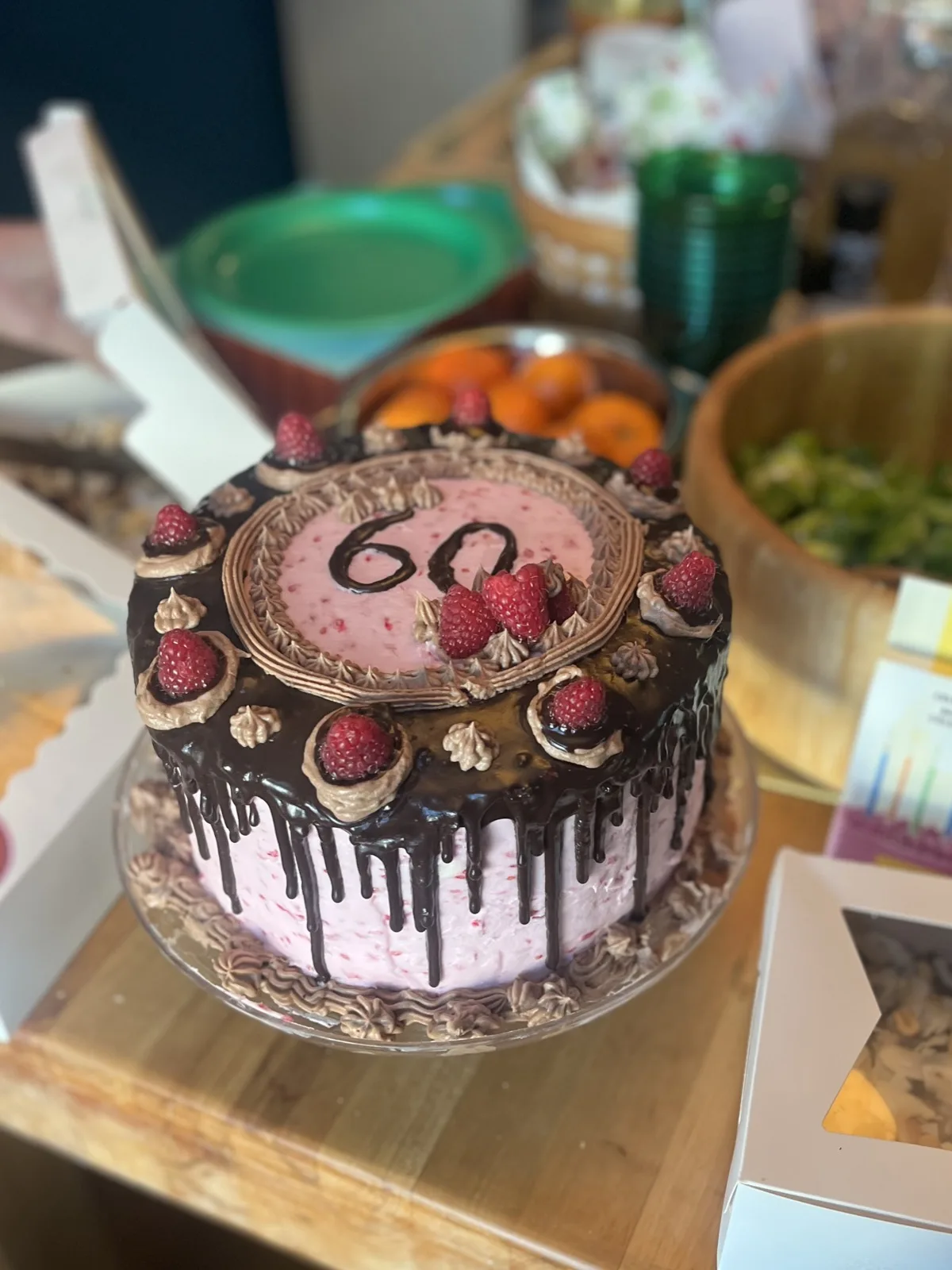 Raspberry buttercream cake with chocolate drip, fresh raspberries, and '60' piped on top